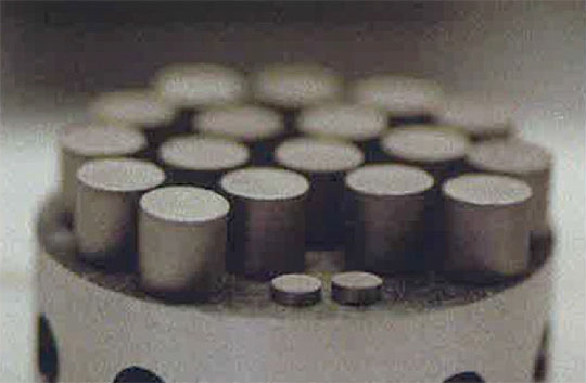 . Enriched UN/U3Si2 pellets (8.4 mm right cylinders) and thermophysical property witness samples (foreground) fabricated in   the MST-7 