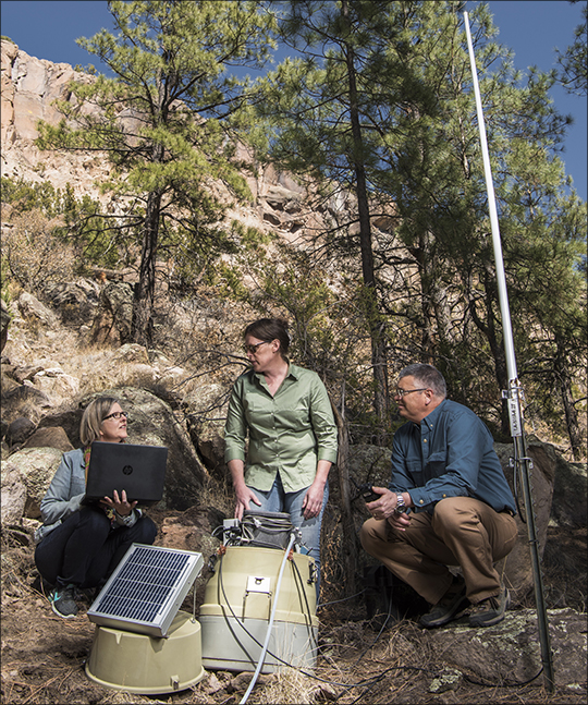 Photo. (Left to right): Janette Frigo, Alex Saari, and Jim Krone configure a Stormwater Runoff sensor node in the field.