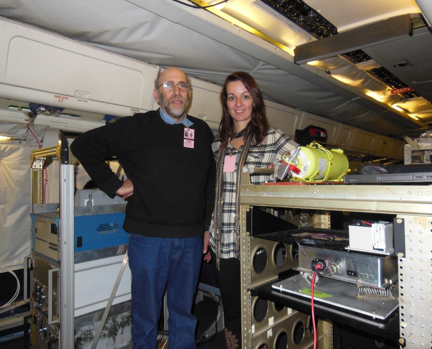 Steve Wender (P-27) and Suzanne Nowicki (ISR-1) are shown in the cabin of a NASA DC-8 aircraft for testing. The Tinman instrument is in the rack with a red ethernet cable connected to it.